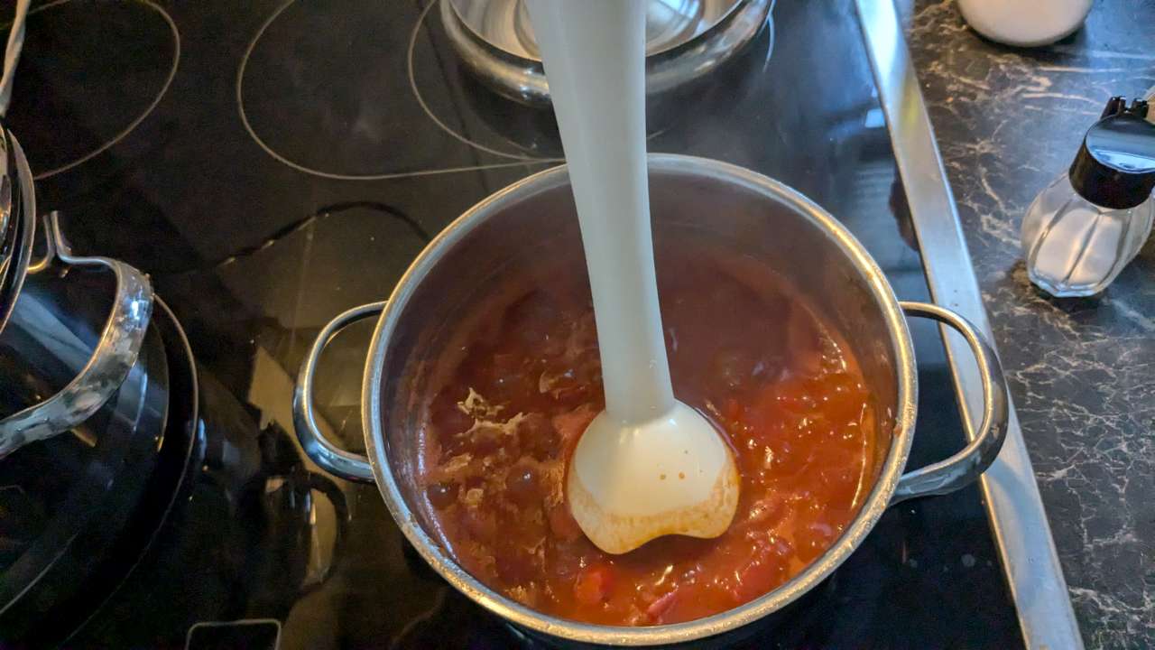 Weißer Stabmixer in der Tomatensoße in einem Topf