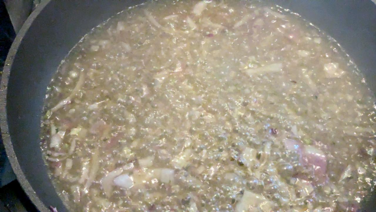 Gemüsebrühe mit Schalottenstücke kocht in einer Pfanne